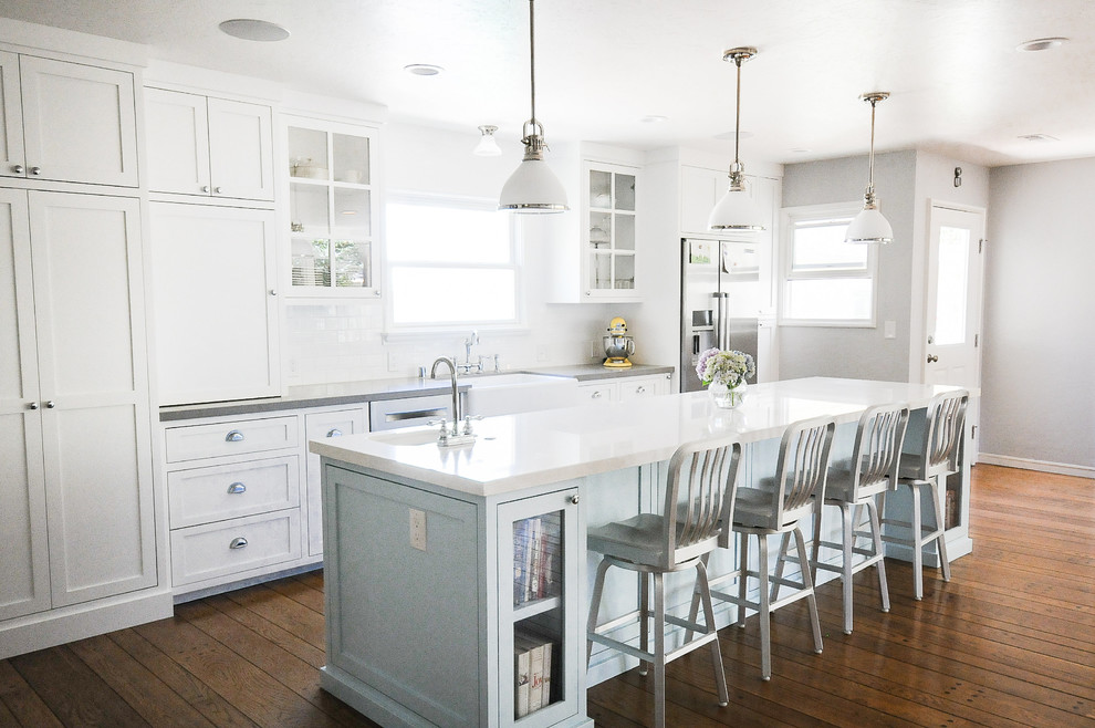 This is an example of a mid-sized country eat-in kitchen in Sacramento with a farmhouse sink, glass-front cabinets, white cabinets, quartzite benchtops, white splashback, subway tile splashback, stainless steel appliances, medium hardwood floors and with island.