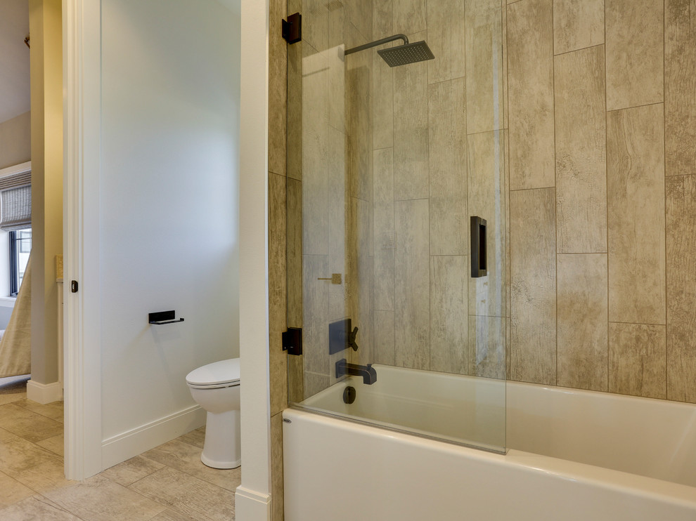 Photo of a mid-sized country kids bathroom in Portland with shaker cabinets, white cabinets, a drop-in tub, a shower/bathtub combo, a one-piece toilet, brown tile, ceramic tile, white walls, porcelain floors, an undermount sink, engineered quartz benchtops and a sliding shower screen.