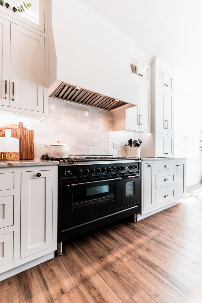 Inspiration for a large transitional l-shaped light wood floor open concept kitchen remodel with an undermount sink, shaker cabinets, white cabinets, quartzite countertops, multicolored backsplash, porcelain backsplash, stainless steel appliances and an island