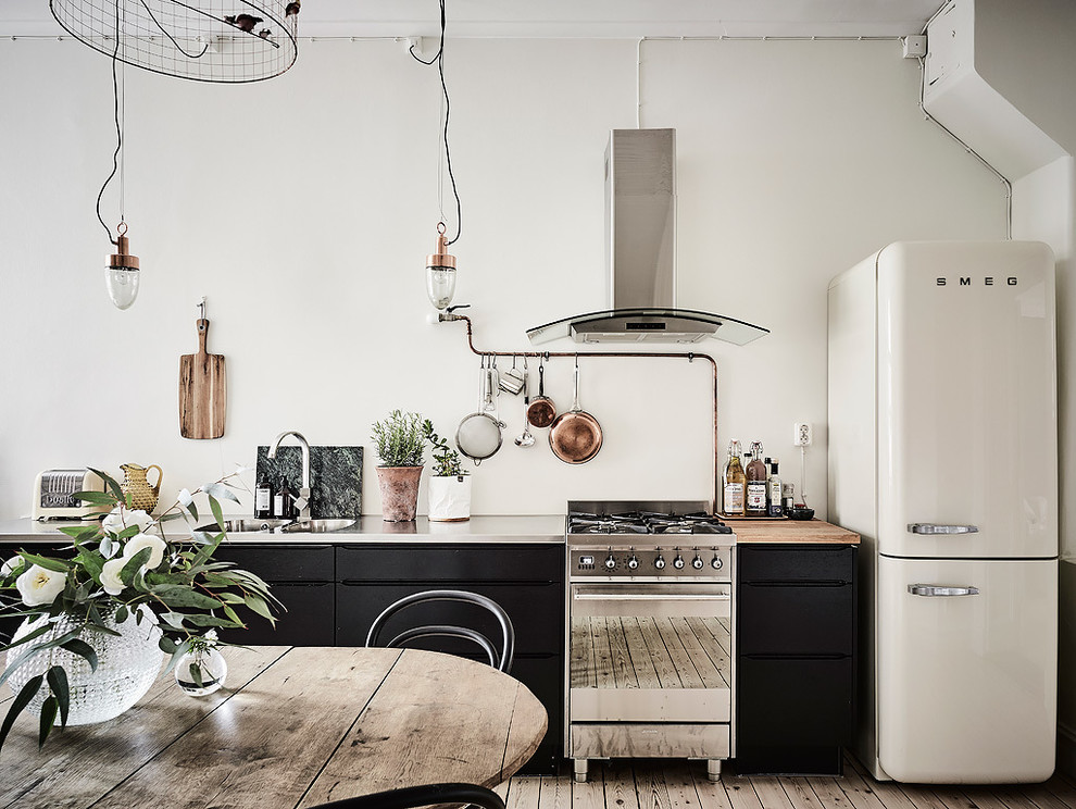 This is an example of a large industrial single-wall eat-in kitchen in Gothenburg with a double-bowl sink, flat-panel cabinets, black cabinets, stainless steel benchtops, stainless steel appliances, light hardwood floors and no island.