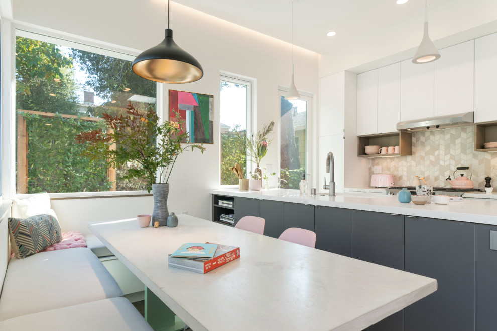 This is an example of a contemporary galley eat-in kitchen in San Francisco with flat-panel cabinets, white cabinets, beige splashback, mosaic tile splashback, stainless steel appliances, with island and white benchtop.