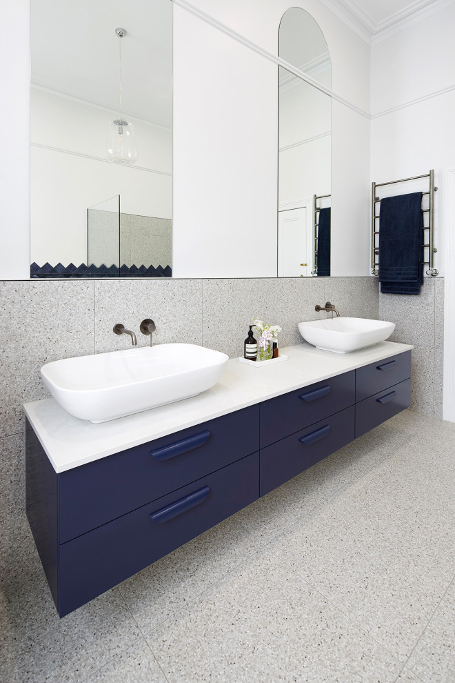 Photo of a large contemporary kids bathroom in Melbourne with flat-panel cabinets, blue cabinets, a freestanding tub, an open shower, a wall-mount toilet, gray tile, multi-coloured walls, terrazzo floors, a vessel sink, engineered quartz benchtops, multi-coloured floor, an open shower and white benchtops.