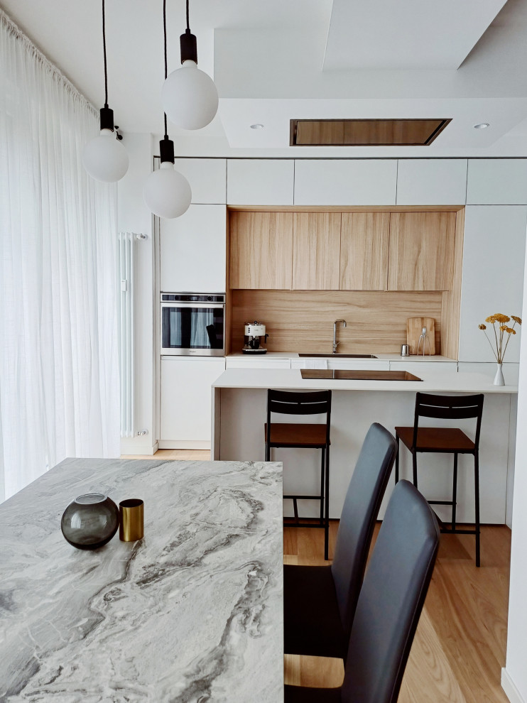 Inspiration for a medium sized scandinavian galley open plan kitchen in Milan with a submerged sink, flat-panel cabinets, white cabinets, composite countertops, wood splashback, stainless steel appliances, light hardwood flooring, an island and white worktops.