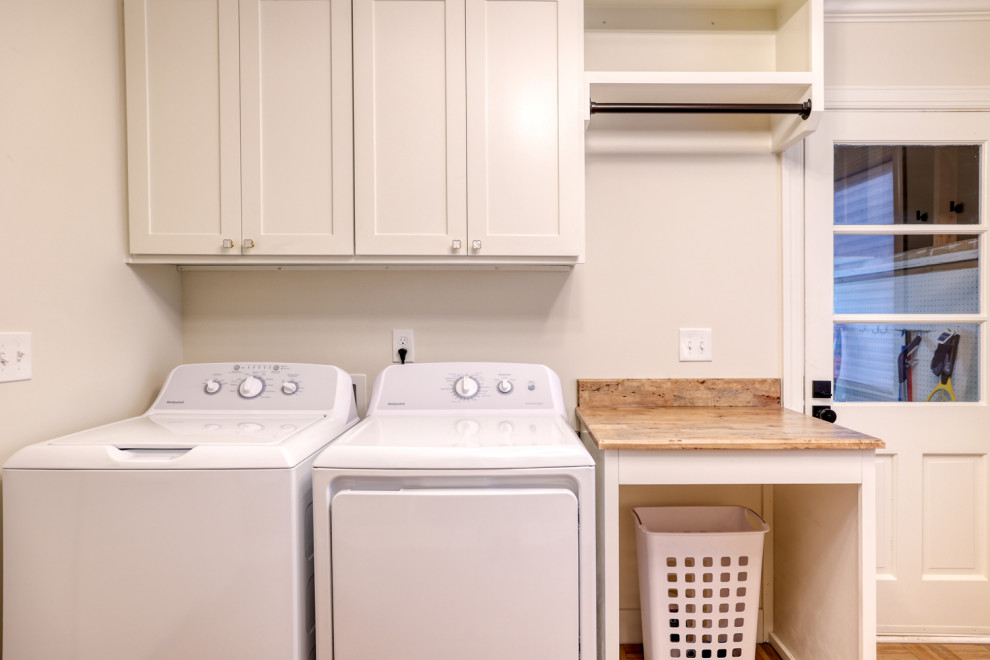 Exempel på en 50 tals grå grått tvättstuga, med skåp i shakerstil, vita skåp, träbänkskiva, vita väggar, ljust trägolv, en tvättmaskin och torktumlare bredvid varandra och grått golv