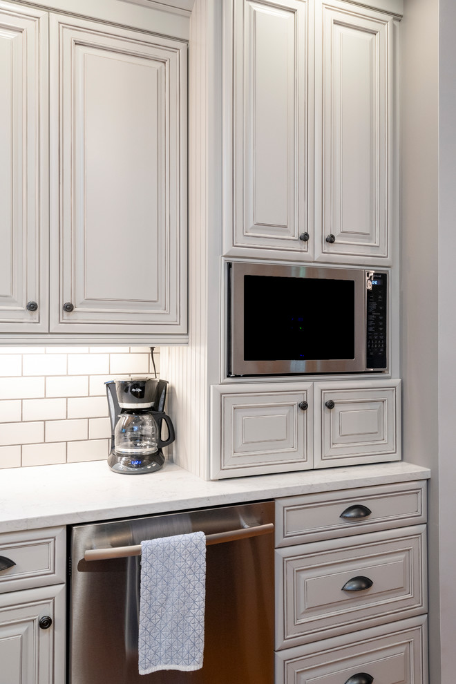 Mid-sized transitional l-shaped medium tone wood floor and red floor eat-in kitchen photo with an undermount sink, raised-panel cabinets, gray cabinets, quartz countertops, gray backsplash, subway tile backsplash, stainless steel appliances, an island and white countertops