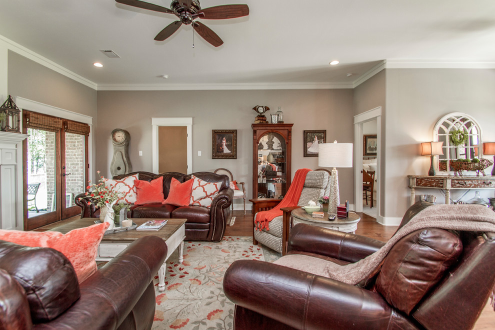 This is an example of a large country open concept living room in Little Rock with grey walls, medium hardwood floors, a standard fireplace, a wall-mounted tv, brown floor and a stone fireplace surround.