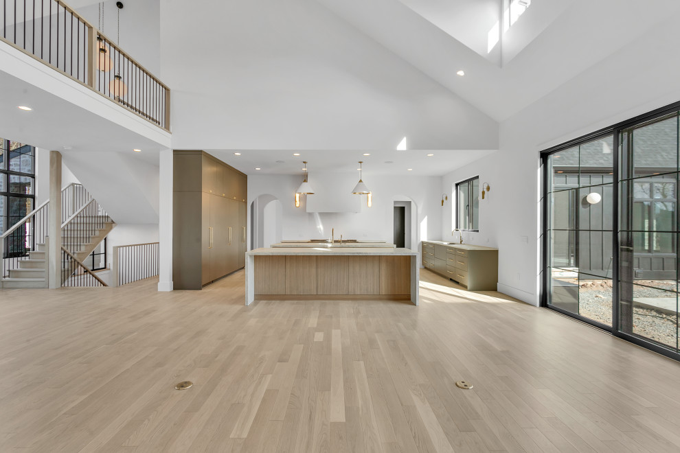 This is an example of a large classic u-shaped open plan kitchen in Other with a submerged sink, flat-panel cabinets, light wood cabinets, quartz worktops, white splashback, integrated appliances, light hardwood flooring, multiple islands, beige floors, beige worktops and a vaulted ceiling.