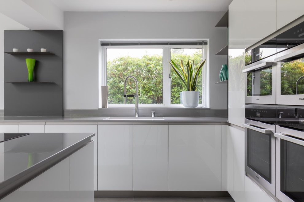 Large contemporary open plan kitchen in Sussex with flat-panel cabinets, white cabinets, solid surface benchtops, grey splashback, with island and grey benchtop.