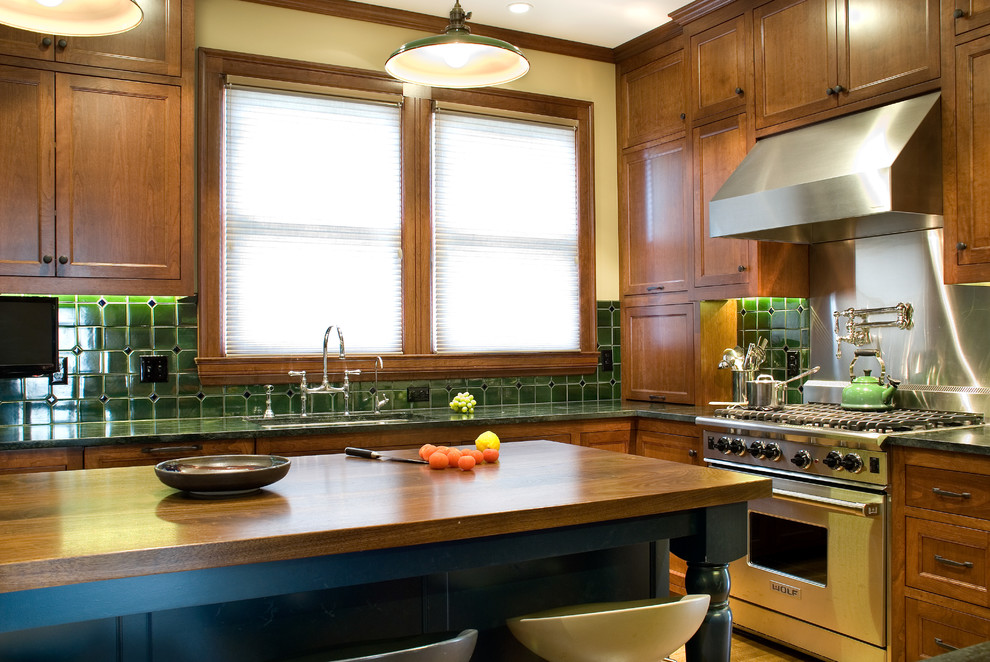 This is an example of a mid-sized traditional l-shaped eat-in kitchen in Minneapolis with an undermount sink, recessed-panel cabinets, medium wood cabinets, soapstone benchtops, green splashback, mosaic tile splashback, stainless steel appliances, medium hardwood floors, with island, brown floor and green benchtop.