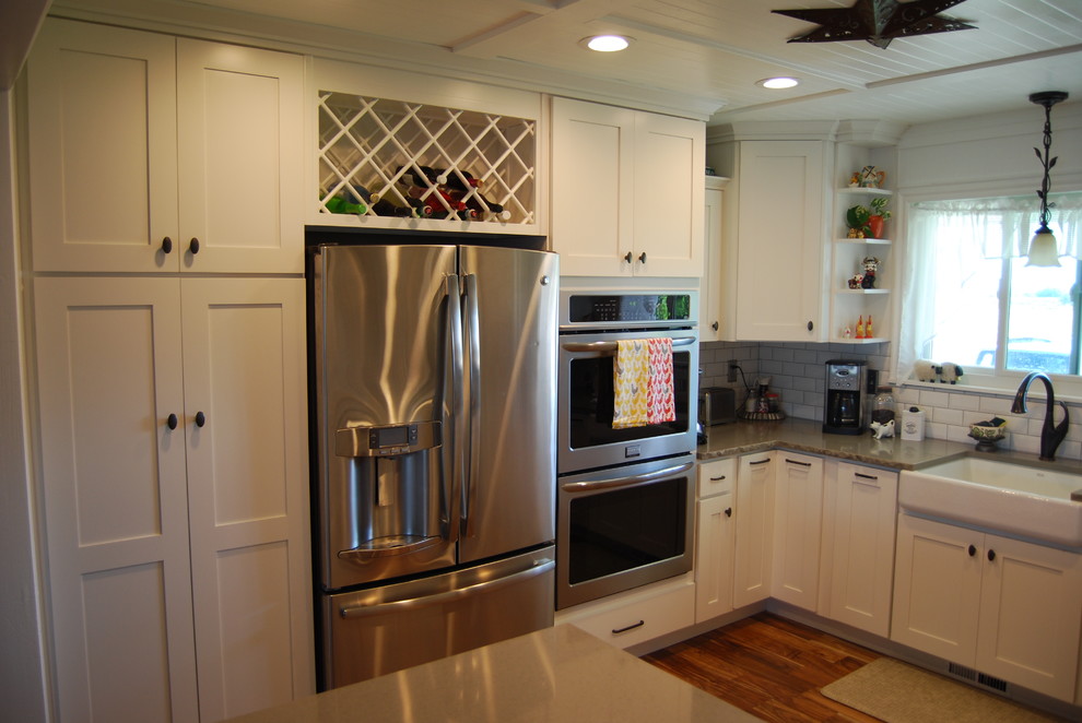Eat-in kitchen - mid-sized transitional u-shaped dark wood floor and brown floor eat-in kitchen idea with a farmhouse sink, shaker cabinets, white cabinets, white backsplash, subway tile backsplash, stainless steel appliances and a peninsula