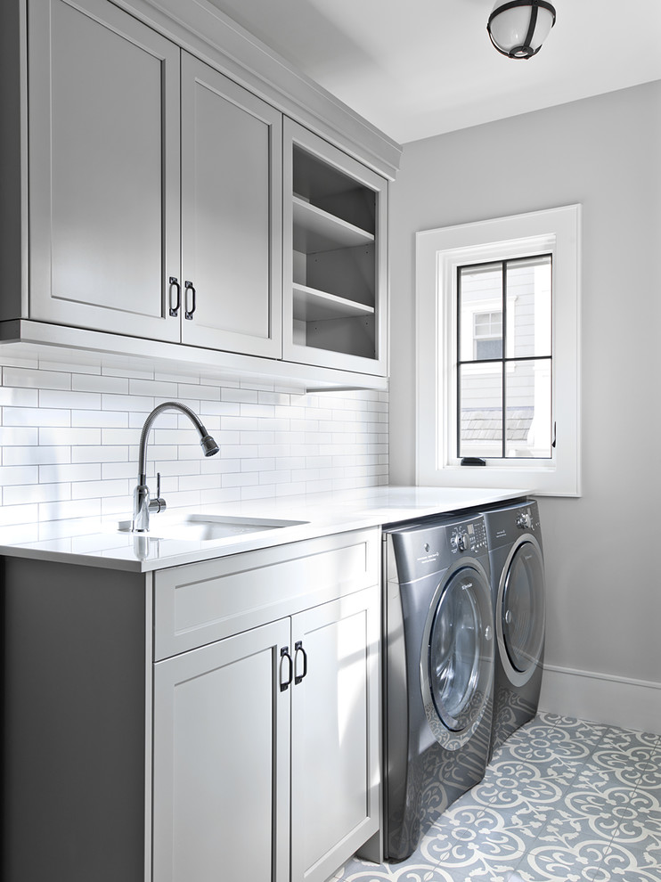 Inspiration for a country single-wall dedicated laundry room in Chicago with an undermount sink, recessed-panel cabinets, grey cabinets, grey walls, a side-by-side washer and dryer, grey floor and white benchtop.