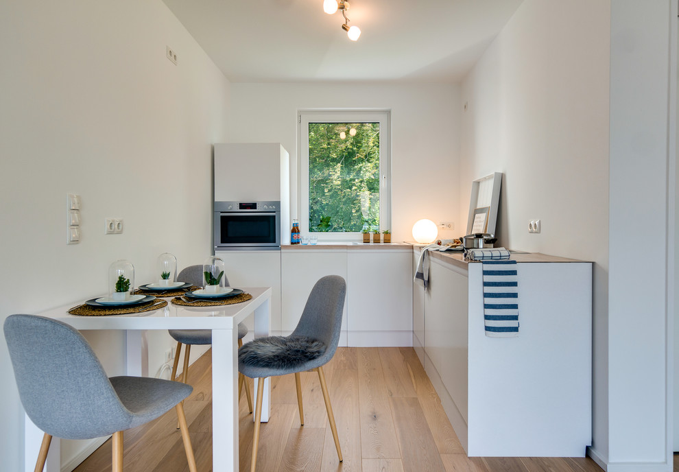 Small scandinavian l-shaped open plan kitchen in Hamburg with flat-panel cabinets, white cabinets, stainless steel appliances, medium hardwood floors, no island and brown floor.