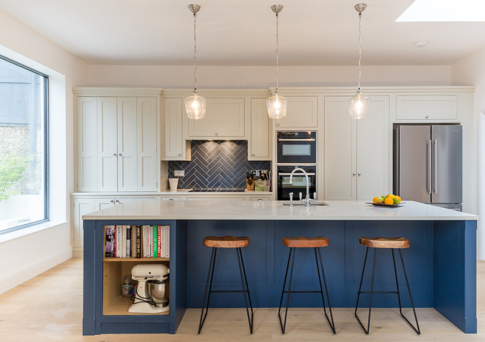 Photo of a mid-sized transitional single-wall kitchen in London with an undermount sink, recessed-panel cabinets, blue splashback, subway tile splashback, stainless steel appliances, light hardwood floors, with island, beige floor and white benchtop.