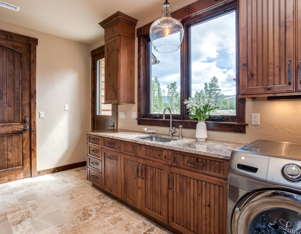 This is an example of a large traditional galley utility room in Denver with an undermount sink, beaded inset cabinets, medium wood cabinets, granite benchtops, beige walls, porcelain floors, a side-by-side washer and dryer and beige floor.