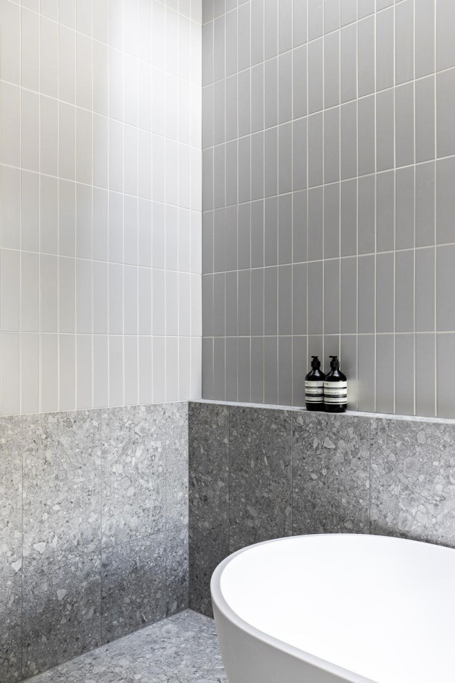 This is an example of an industrial bathroom in Sydney with white cabinets, a freestanding tub, gray tile, ceramic tile, grey walls, porcelain floors, tile benchtops, grey floor, a niche and a double vanity.