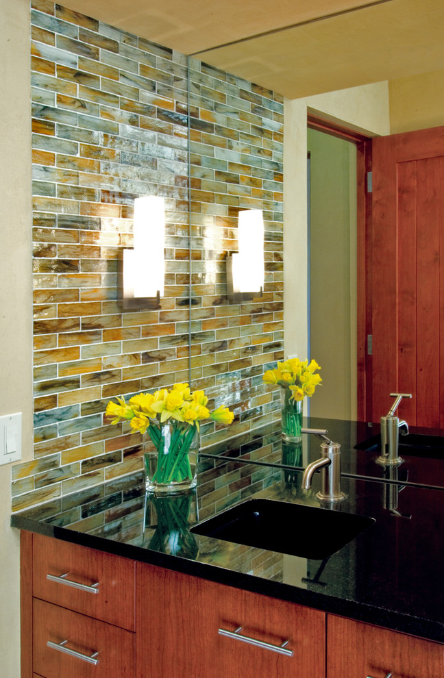 Photo of a mid-sized modern powder room in Albuquerque with an undermount sink, flat-panel cabinets, medium wood cabinets, granite benchtops, multi-coloured tile and glass tile.