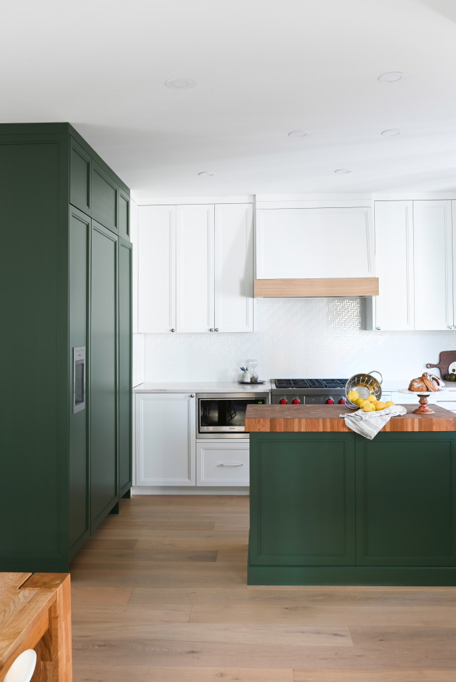 This is an example of a small traditional u-shaped eat-in kitchen in Vancouver with a farmhouse sink, shaker cabinets, green cabinets, quartz benchtops, white splashback, mosaic tile splashback, stainless steel appliances, medium hardwood floors, with island and white benchtop.