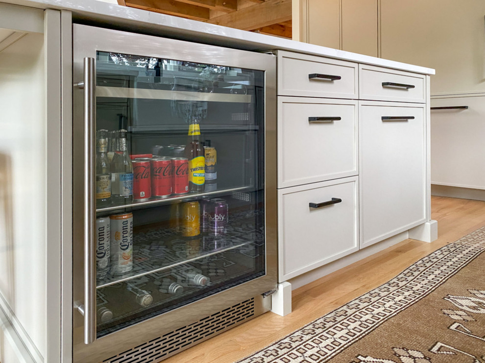 Transitional l-shaped light wood floor and exposed beam kitchen photo in Boston with a farmhouse sink, shaker cabinets, gray cabinets, quartz countertops, white backsplash, ceramic backsplash, paneled appliances, an island and white countertops