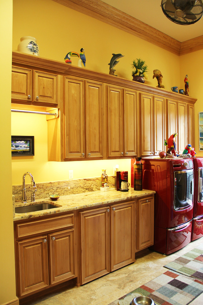 Photo of a large tropical galley utility room in New Orleans with an undermount sink, raised-panel cabinets, medium wood cabinets, yellow walls and a side-by-side washer and dryer.