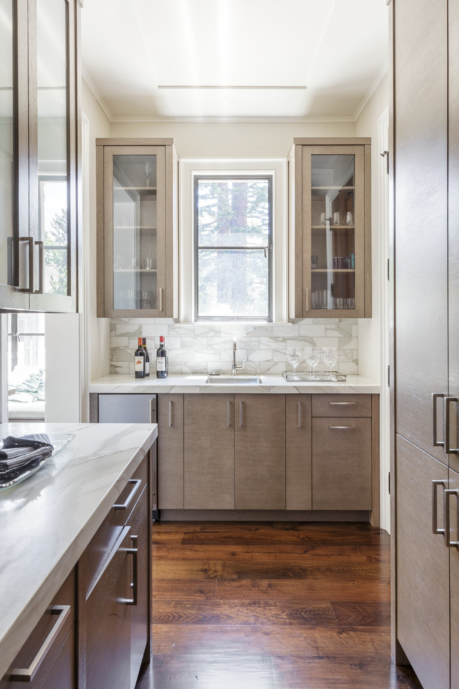 This is an example of a large transitional galley home bar in San Francisco with an undermount sink, flat-panel cabinets, brown cabinets, marble benchtops, grey splashback and dark hardwood floors.