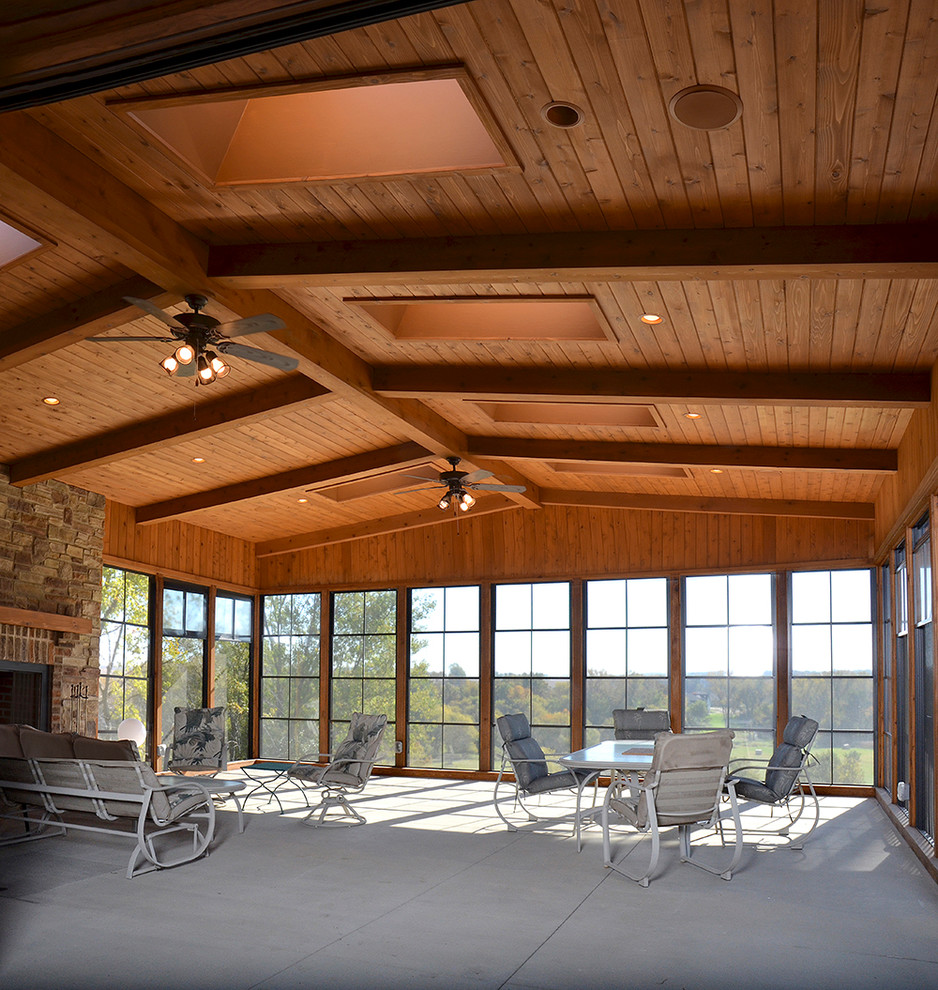 Photo of a large sunroom in Cedar Rapids with concrete floors, a standard fireplace and a stone fireplace surround.