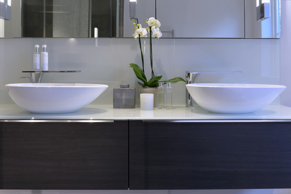 Photo of a mid-sized contemporary kids bathroom in Gloucestershire with dark wood cabinets, glass sheet wall, a vessel sink and glass benchtops.