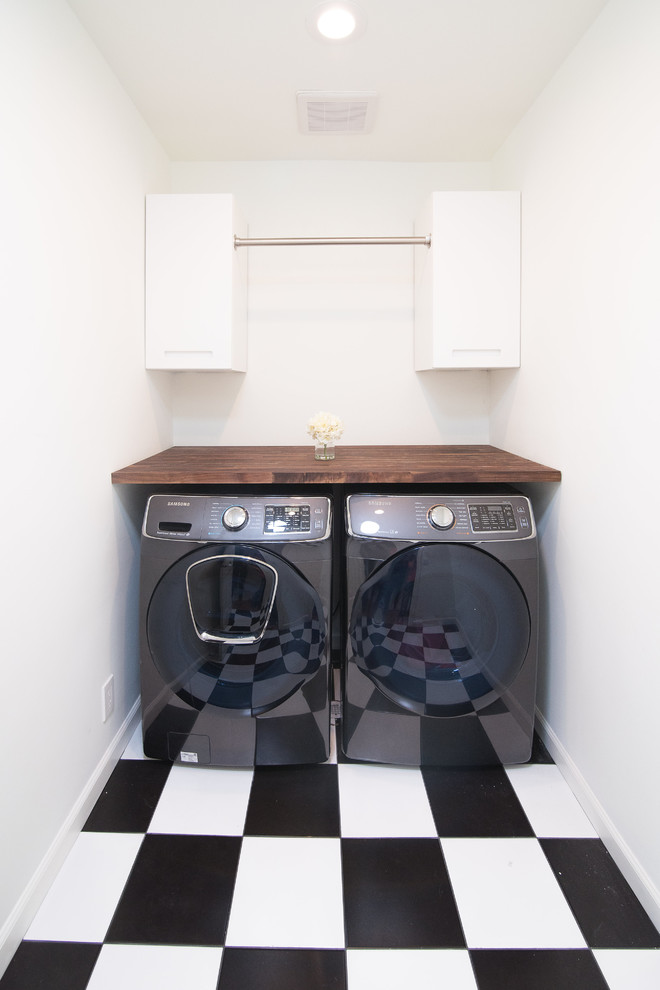 Design ideas for a mid-sized transitional single-wall dedicated laundry room in Los Angeles with flat-panel cabinets, white cabinets, wood benchtops, white walls, linoleum floors, a side-by-side washer and dryer, multi-coloured floor and brown benchtop.