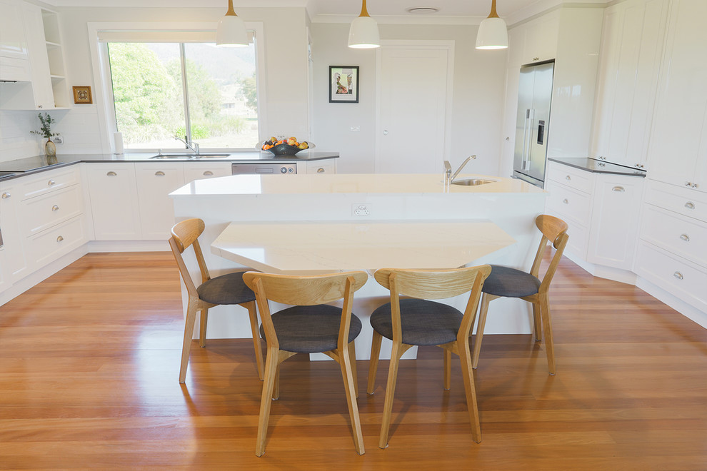 Design ideas for a large transitional galley eat-in kitchen in Sydney with a double-bowl sink, flat-panel cabinets, white cabinets, quartz benchtops, white splashback, ceramic splashback, stainless steel appliances, light hardwood floors, with island, brown floor and white benchtop.