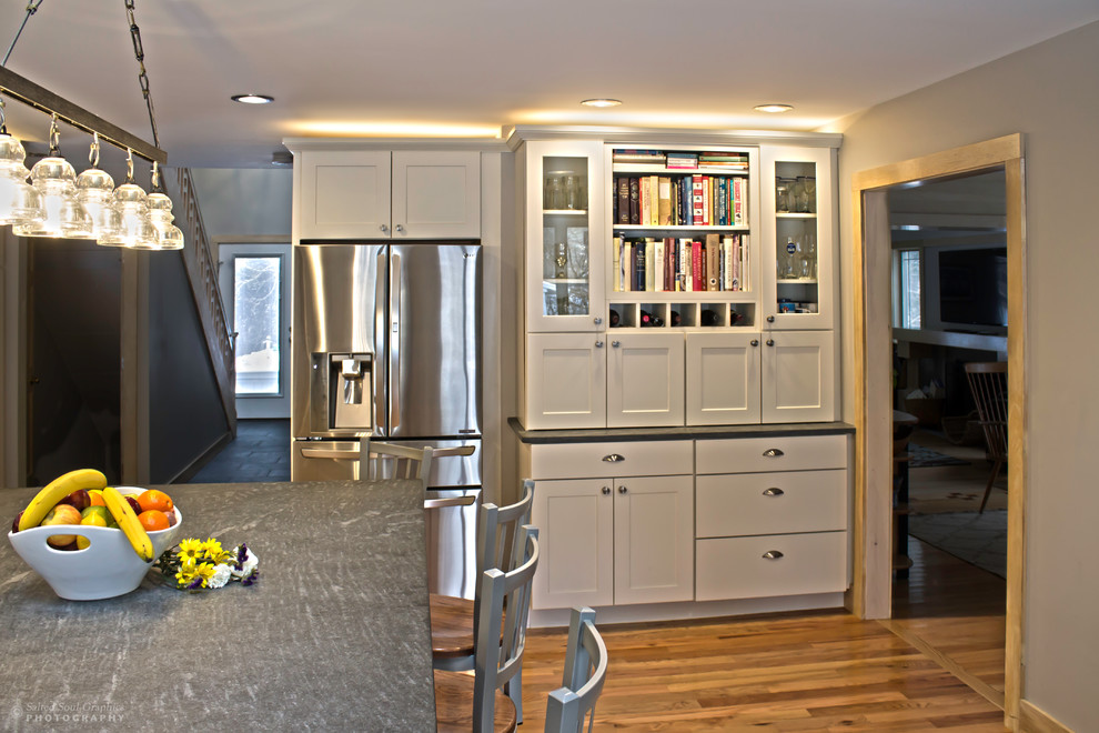 Large mountain style l-shaped light wood floor open concept kitchen photo in Burlington with an undermount sink, shaker cabinets, white cabinets, soapstone countertops, multicolored backsplash, glass tile backsplash, stainless steel appliances and an island