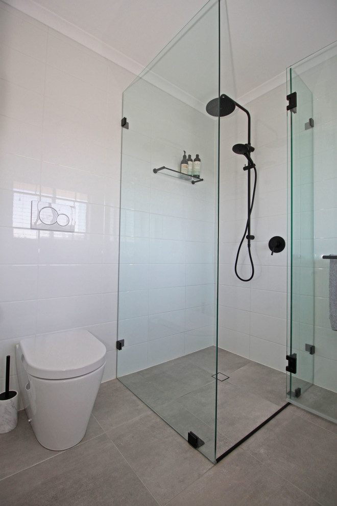 Small modern kids bathroom in Brisbane with flat-panel cabinets, light wood cabinets, a freestanding tub, a curbless shower, a wall-mount toilet, white tile, ceramic tile, white walls, porcelain floors, an integrated sink, solid surface benchtops, grey floor, a hinged shower door and white benchtops.