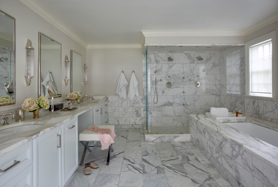 This is an example of an expansive transitional master bathroom in New York with an undermount sink, raised-panel cabinets, white cabinets, marble benchtops, an undermount tub, a corner shower, a one-piece toilet, white tile, stone tile, grey walls and marble floors.