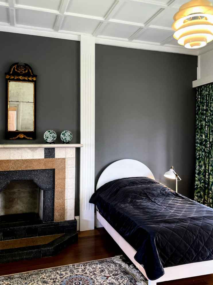 Пример оригинального дизайна: гостевая спальня среднего размера, (комната для гостей) в викторианском стиле с серыми стенами, темным паркетным полом, стандартным камином, фасадом камина из камня, коричневым полом, кессонным потолком и кирпичными стенами