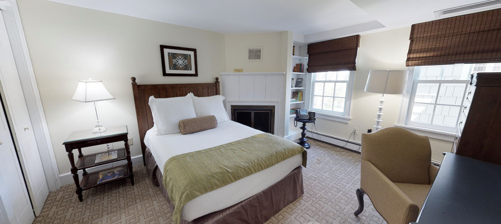 This is an example of a small eclectic guest bedroom with beige walls, carpet, a standard fireplace, a wood fireplace surround and grey floor.