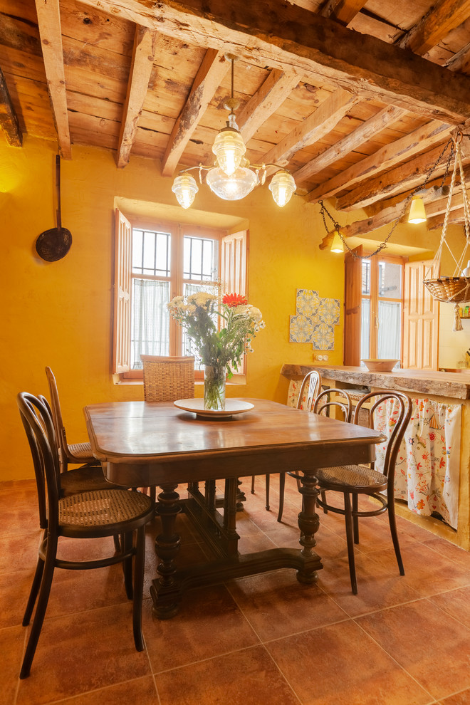 Country kitchen/dining combo in Madrid with yellow walls, no fireplace and brown floor.