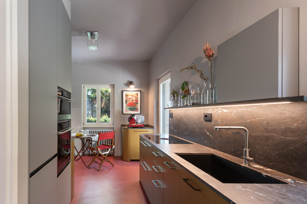 This is an example of a mid-sized midcentury open plan kitchen in Other with a single-bowl sink, flat-panel cabinets, grey cabinets, granite benchtops, grey splashback, glass sheet splashback, stainless steel appliances, concrete floors, red floor and black benchtop.