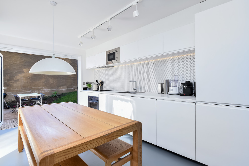 Photo of a mid-sized modern galley eat-in kitchen in London with a single-bowl sink, flat-panel cabinets, white cabinets, laminate benchtops, white splashback, ceramic splashback, stainless steel appliances, linoleum floors, no island, grey floor and white benchtop.