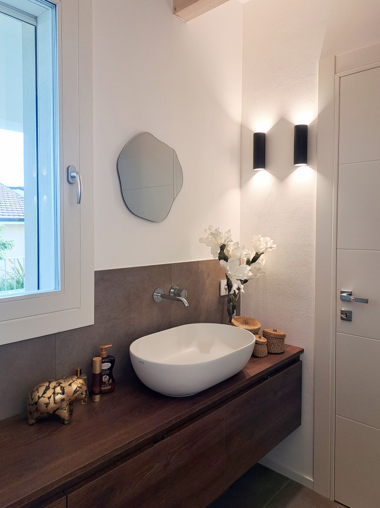 Design ideas for a medium sized contemporary ensuite bathroom in Other with dark wood cabinets, a freestanding bath, an alcove shower, a two-piece toilet, brown tiles, porcelain tiles, white walls, porcelain flooring, a vessel sink, wooden worktops, brown floors, a hinged door, a single sink, a floating vanity unit and exposed beams.