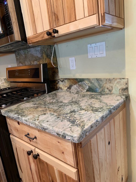 Example of a mid-sized mountain style medium tone wood floor and brown floor open concept kitchen design with an undermount sink, flat-panel cabinets, light wood cabinets, granite countertops, gray backsplash, stone slab backsplash, stainless steel appliances and gray countertops