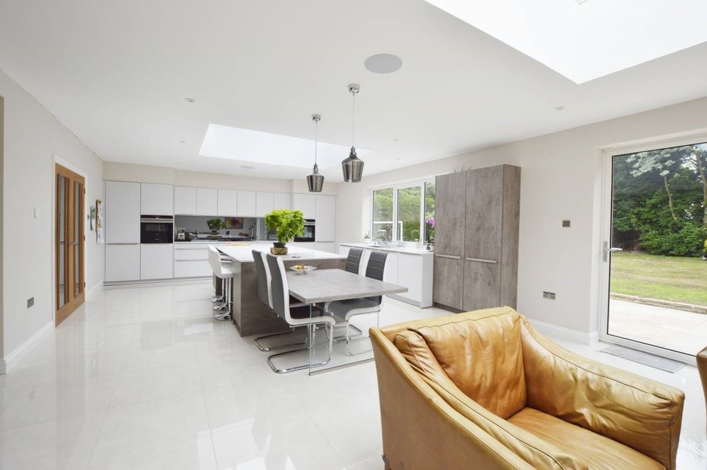 Large contemporary l-shaped open plan kitchen in Other with an integrated sink, flat-panel cabinets, grey cabinets, metallic splashback, mirror splashback, stainless steel appliances, porcelain floors, multiple islands, white floor, white benchtop and coffered.