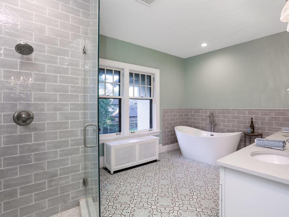 This is an example of a large traditional master bathroom in Detroit with white cabinets, a freestanding tub, a corner shower, gray tile, subway tile, green walls, ceramic floors, an undermount sink, engineered quartz benchtops, multi-coloured floor, a hinged shower door and white benchtops.
