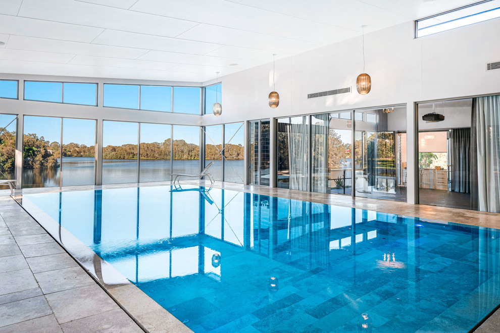 This is an example of a contemporary indoor rectangular infinity pool in Brisbane with a pool house and natural stone pavers.