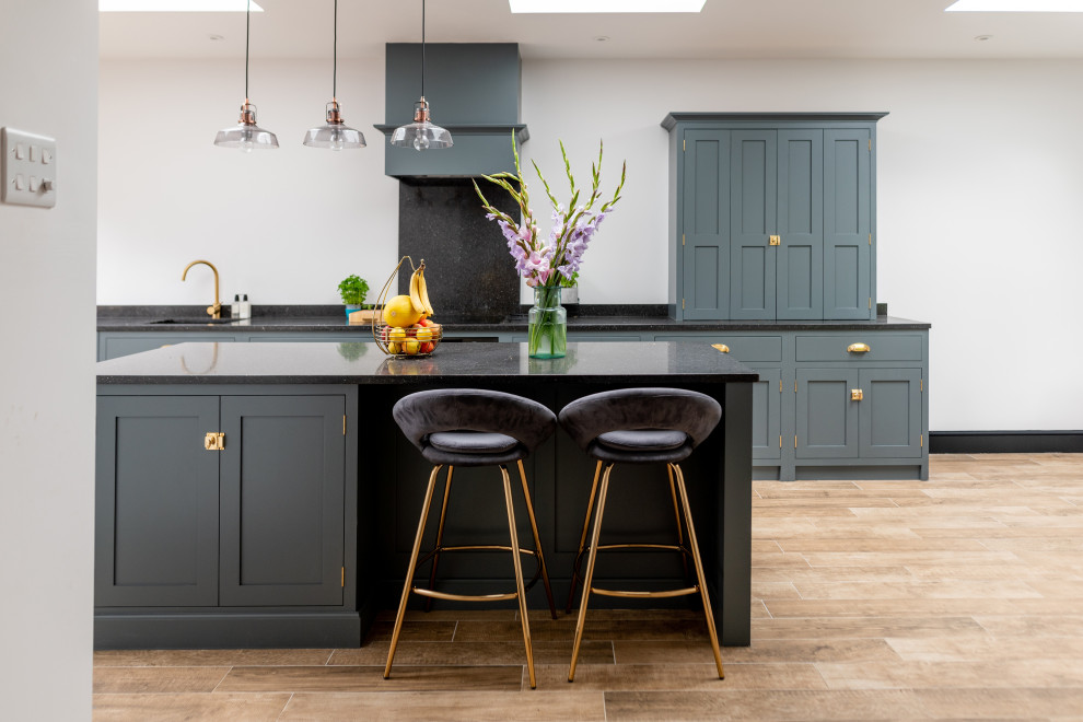 Inspiration for a mid-sized transitional galley open plan kitchen in Surrey with blue cabinets, quartzite benchtops, light hardwood floors, with island, black benchtop, an undermount sink, shaker cabinets and beige floor.