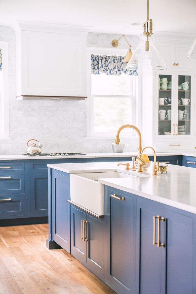 Inspiration for a large transitional kitchen in Philadelphia with a farmhouse sink, shaker cabinets, blue cabinets, white splashback, marble splashback, stainless steel appliances, medium hardwood floors, with island, brown floor and white benchtop.