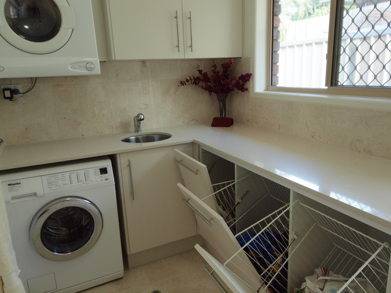Contemporary l-shaped dedicated laundry room in Brisbane with an undermount sink, beige cabinets, quartz benchtops, marble floors and a stacked washer and dryer.