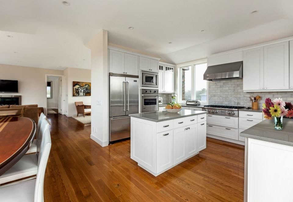 Design ideas for a mid-sized beach style u-shaped eat-in kitchen in New York with a drop-in sink, shaker cabinets, white cabinets, granite benchtops, multi-coloured splashback, stone tile splashback, stainless steel appliances, medium hardwood floors, with island and brown floor.