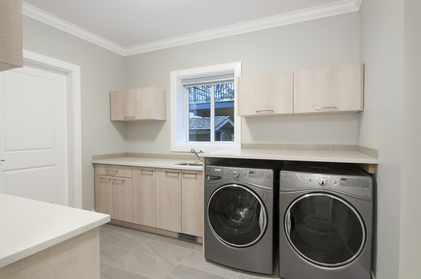 This is an example of a mid-sized contemporary galley dedicated laundry room in Vancouver with an undermount sink, flat-panel cabinets, light wood cabinets, quartz benchtops, grey walls, porcelain floors, a side-by-side washer and dryer and grey floor.