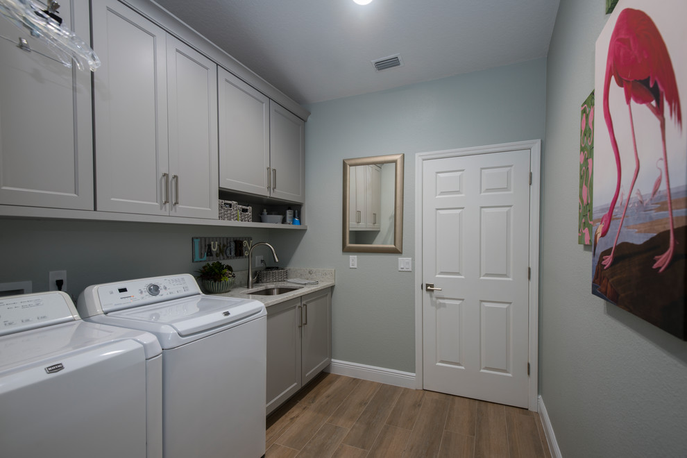 Design ideas for a mid-sized transitional single-wall laundry room in Orlando with an undermount sink, recessed-panel cabinets, grey cabinets, quartzite benchtops, grey walls, medium hardwood floors, a side-by-side washer and dryer and brown floor.