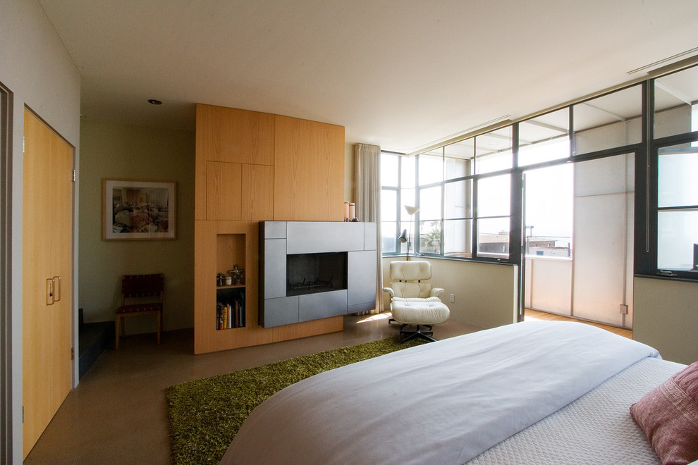 Modern master bedroom in Los Angeles with beige walls, a hanging fireplace, a stone fireplace surround and brown floor.