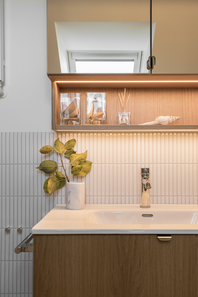 Duschbad With hellen Holzschränken, Einbaubadewanne, bodengleicher Dusche, Wandtoilette mit Spülkasten, weißen Fliesen, Keramikfliesen, weißer Wandfarbe, Porzellan-Bodenfliesen, grauem Boden, weißer Waschtischplatte, Wäscheaufbewahrung, Einzelwaschbecken and eingebautem Waschtisch in Berlin