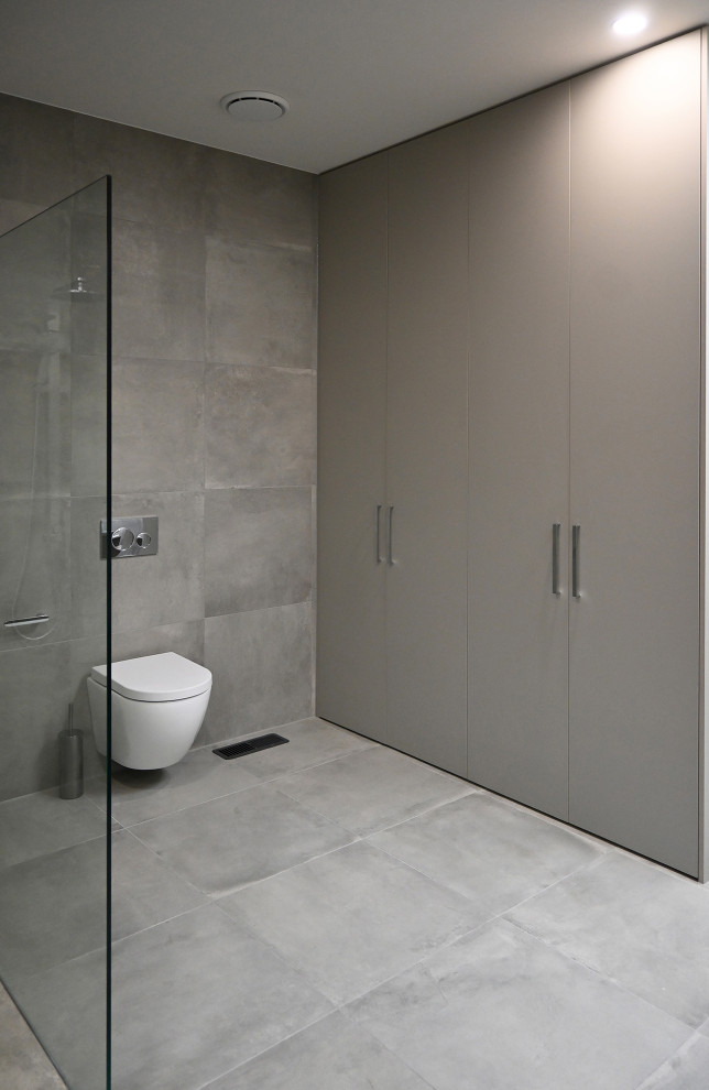 Design ideas for a large contemporary master bathroom in Melbourne with raised-panel cabinets, brown cabinets, an open shower, a wall-mount toilet, gray tile, porcelain tile, grey walls, porcelain floors, tile benchtops, grey floor, an open shower, grey benchtops, a laundry, a double vanity and a floating vanity.
